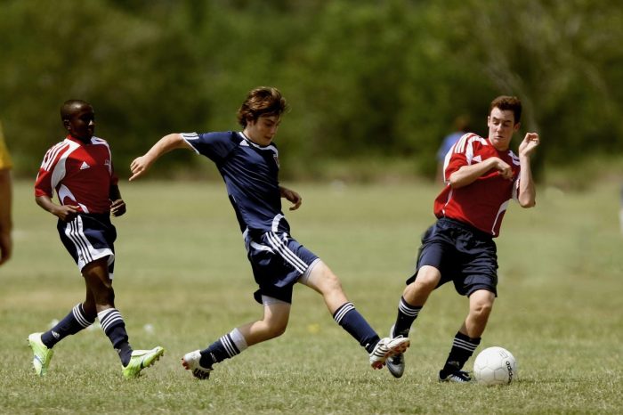 Three players playing soccer while people are doing their sports betting types